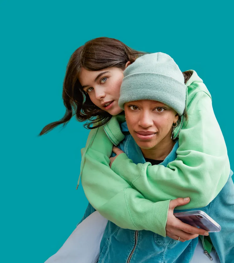 A teenager piggybacks another teenager, holding a smart phone