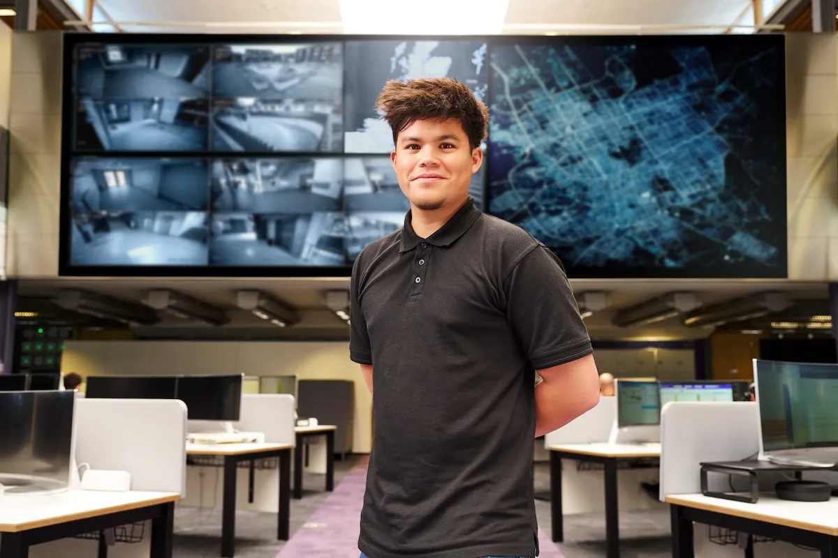 A young person stands in front of large screens in an office environment