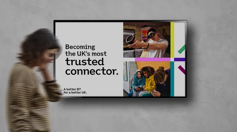 A woman walks past a television displaying a presentation on BT's refreshed strategy