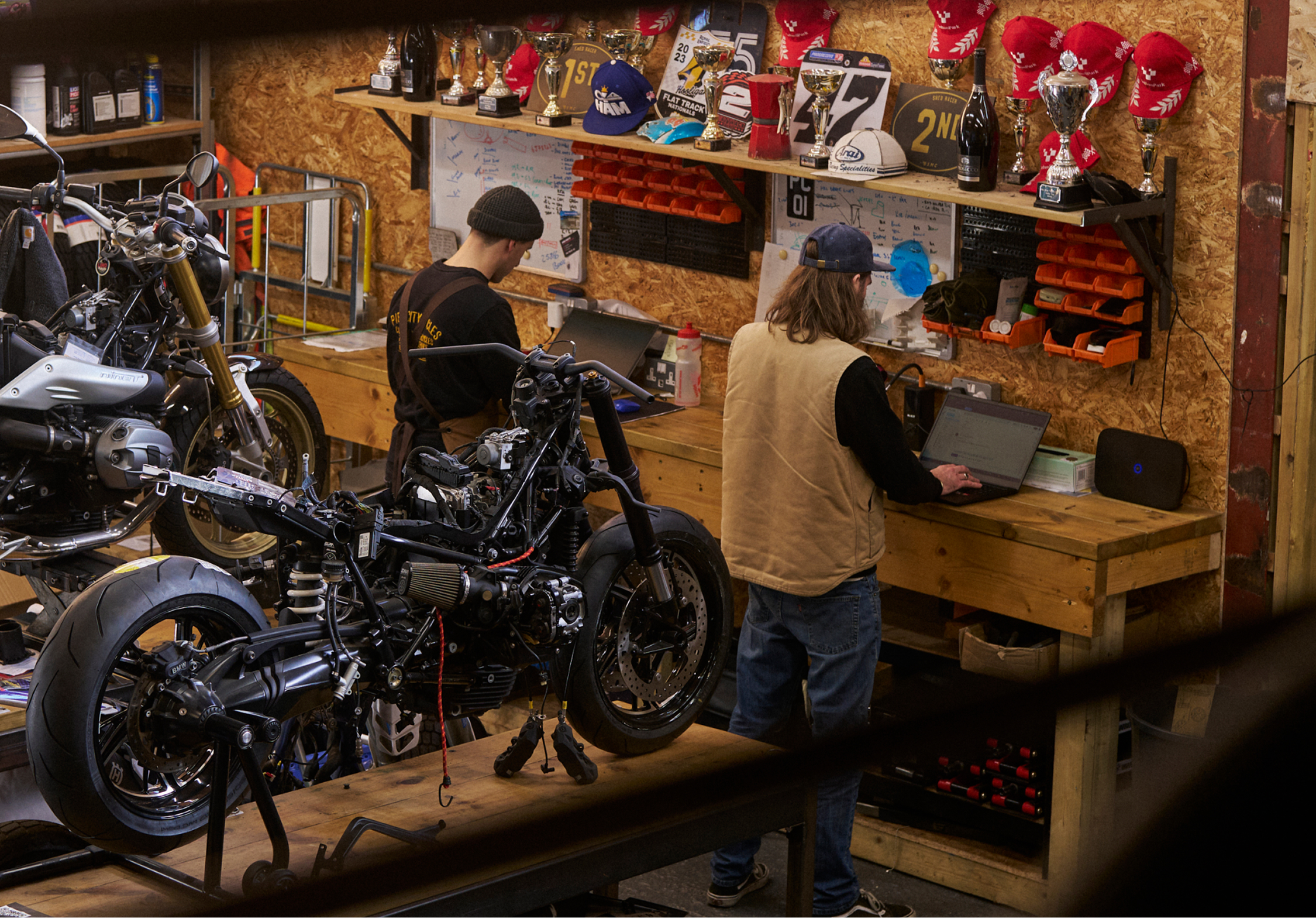 Two people in a motorbike workshop on laptops
