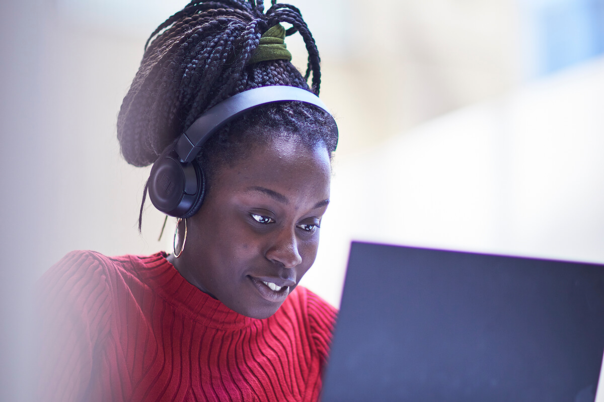 Girl with red sweater wearing a headset and working on a laptop