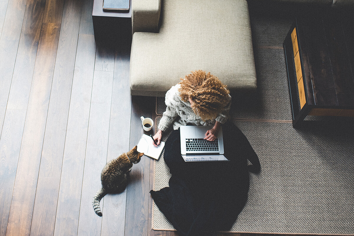 Woman sitting on a floor working on a laptop with a cat