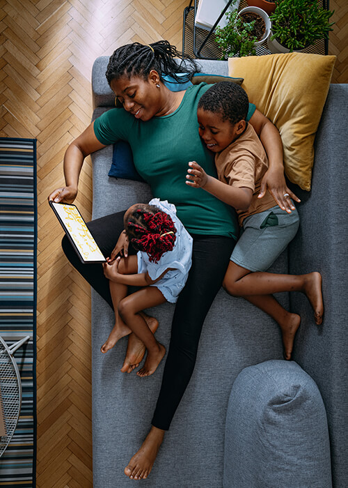 Mother and two children lying on a sofa looking at a tablet