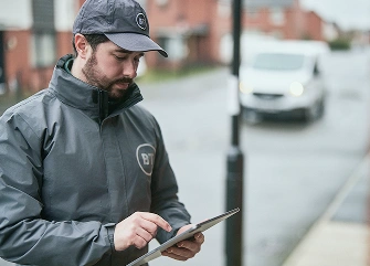A BT broadband engineer using a tablet outdoors, representing local customer support and technical assistance.