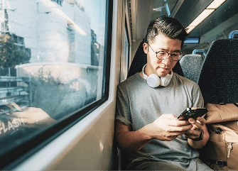 A person using a mobile phone while travelling, representing easy broadband and Wi‑Fi management through an app.