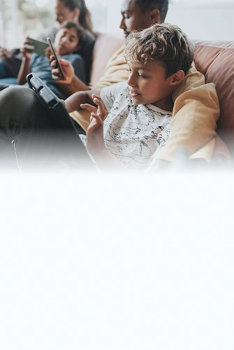 People using multiple devices in a living room, representing online activity across a busy household.