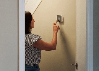 A person adjusting a smart thermostat on a wall, representing connected smart home devices using the home broadband network.